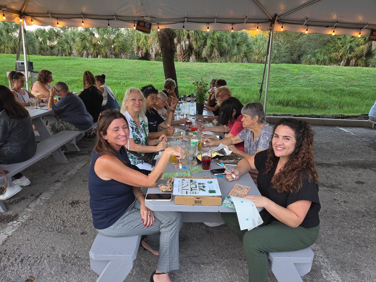 Friends laughing around a picnic table at Plant Bingo, cards out